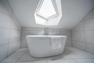 Fenêtre de toit installée dans une salle de bains moderne avec baignoire îlot blanche et carrelage gris clair