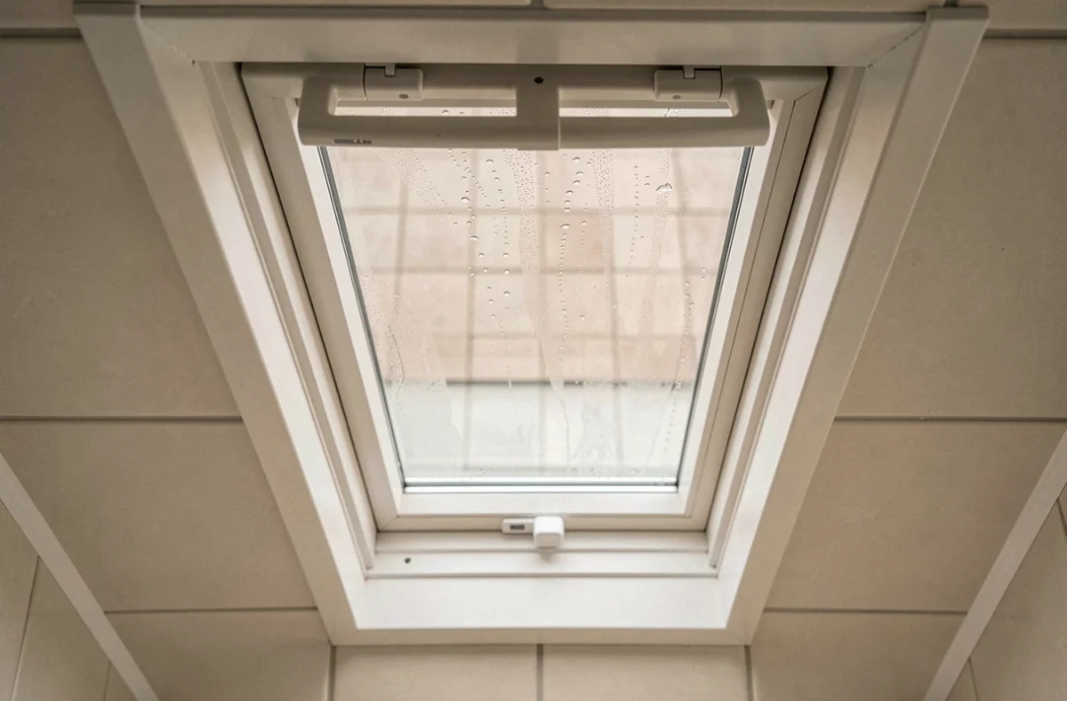 Gros plan sur le cadre PVC d'une fenêtre de toit en salle de bains avec mécanisme d'ouverture et vitre légèrement condensée
