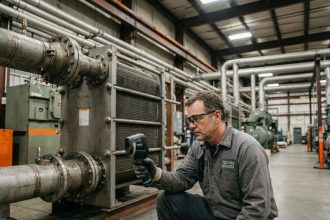 Technicien industriel inspectant un échangeur de chaleur dans une usine moderne, équipement de gestion thermique industrielle